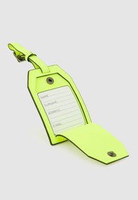 Etichetta per bagagli giallo neon in materiale sintetico con design pieghevole, dotata di porta scheda per nome e indirizzo, fissata da un bottone automatico in metallo.