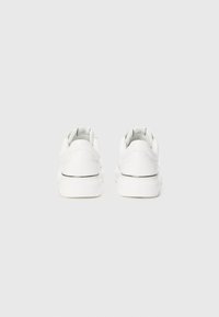 Hvide sneakers med glat læderoverdel, rund tå og lav profil. Har to bageste huller og en kontrasterende sort stribe langs sålen.