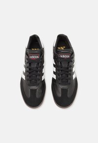 Chaussures de sport noires avec trois bandes blanches. Fabriquées en cuir et en daim, avec un bout arrondi et une semelle en caoutchouc texturée.