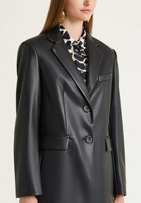 Blazer in pelle nera con design strutturato, chiusura monopetto, due tasche anteriori e una texture liscia e lucida.