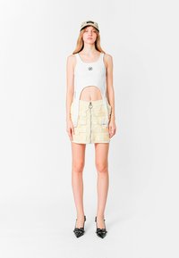 Top de tirantes blanco con laterales recortados, pantalones cortos de cargo beige con bolsillos de parche y cremallera, y tacones de punta negra.