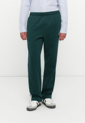 Person wearing dark green sweatpants with elastic waistband, white and black sneakers, and a light blue striped button-up shirt.
