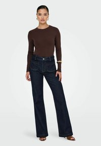 Un haut marron à manches longues associé à un jean large taille haute de couleur bleu foncé, avec des poches avant et arrière, et un bouton supérieur visible.