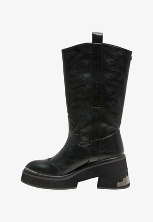 Bota de cuero negro hasta la rodilla con un tacón grueso, que presenta detalles en relieve, una superficie texturada y una asa lateral para facilitar su uso.