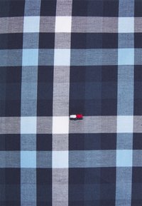 Tela a cuadros en azul marino y azul claro con cuadrados blancos, con un pequeño logo bordado en rojo, blanco y azul en el centro.