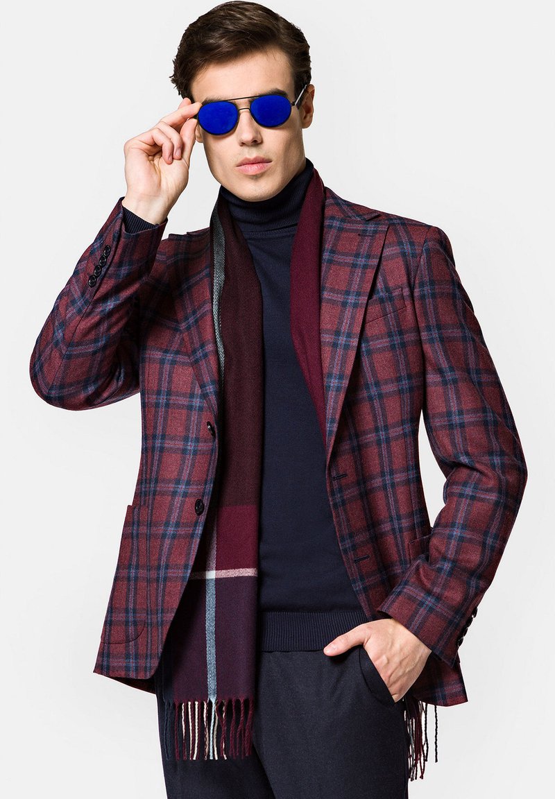 Marynarkę w szkocką kratę w odcieniach burgundowym i granatowym, dopasowaną, założoną na granatowy golf. W zestawie burgundowy szalik i niebieskie okulary przeciwsłoneczne.