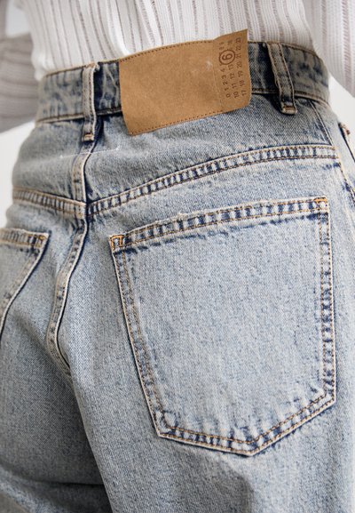 Lys blå denimjeans har høj talje, fem lommer og subtile slidmærker. En tan læderpatch er syet på den bageste talje.