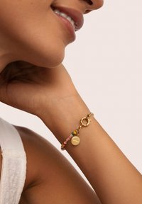 Pulsera de oro que presenta cuentas coloridas en rosa, amarillo y verde. Charm redondo notable con grabado, asegurado por un cierre de langosta.