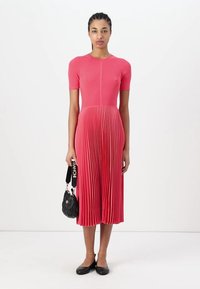 Abito midi in maglina di un brillante colore rosa, con maniche corte, texture a coste e gonna plissettata. Abbinato a una borsa nera e scarpe basse.