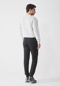 Hanorac gri asociat cu pantaloni jogger negri. Detaliile notabile includ un guler rotund, manșete elastice și un buzunar pe spate la pantaloni.