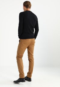 Schwarzer Pullover mit langen Ärmeln, kombiniert mit beige Chinos und schwarzen Stiefeletten. Der Pullover hat ein figurbetontes Design und eine gerippte Textur.