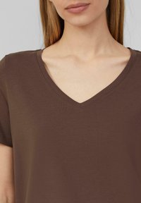 Koffiekleurige V-hals T-shirt van zachte stof met korte mouwen. Glad textuur met een relaxte pasvorm en subtiele stikdetails rond de halslijn.