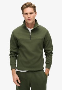 Sudadera de forro polar verde con un cuello alto, cremallera frontal de medio largo y mangas largas; cuenta con una textura suave y bolsillos laterales.