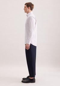 Camicia a maniche lunghe a righe bianche e rosa chiaro, abbinata a pantaloni blu navy e scarpe di pelle nere. La camicia presenta un colletto classico.