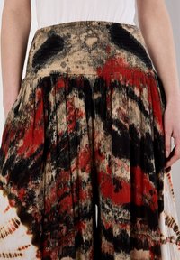 Jupe plissée beige avec des motifs abstraits noirs et rouges. Comprend une taille smockée et un tissu léger et texturé.