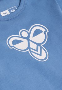 Ljusblå bomullst-shirt med en stor vit fjärilslogotyp med geometriska former och konturer, rund halsringning och mjuk textur.