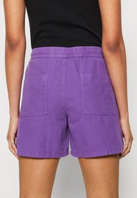 Lila bomullsshorts med elastisk midja, två bakfickor och rak skärning. Slät textur med sömdetaljer.