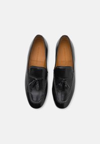 Loafers negri din piele, cu o textură netedă, având decoruri cu franjuri și un design cu margine cusută. Interiorul este din piele bej.