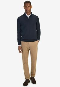 Marinblå zip-up tröja över en vit skjorta med krage, beige byxor och mörkbruna skor. Tröjan har en strukturerad yta och ribbade ärmslut.