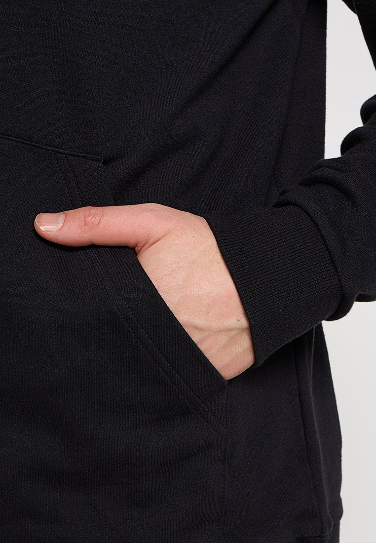 Felpa nera con tasca frontale, polsini a costina e una texture liscia, che mostra una mano appoggiata nella tasca.