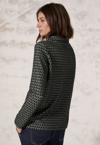 Groene blazer met een geometrisch driehoekpatroon, kraag en lange mouwen, gecombineerd met donkere jeans. Glad textuur en aansluitende pasvorm.