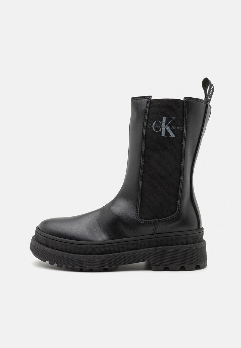 Bottes Chelsea en cuir noir avec semelle épaisse, panneau latéral élastique comportant le logo "cK" Calvin Klein Jeans, et languette à l'arrière.