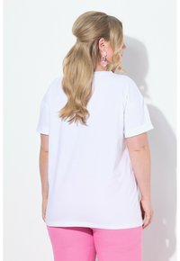 Witte t-shirt met korte mouwen en een losse pasvorm, weergegeven vanuit de achterkant. Gladde katoenmateriaal, gecombineerd met roze broek.