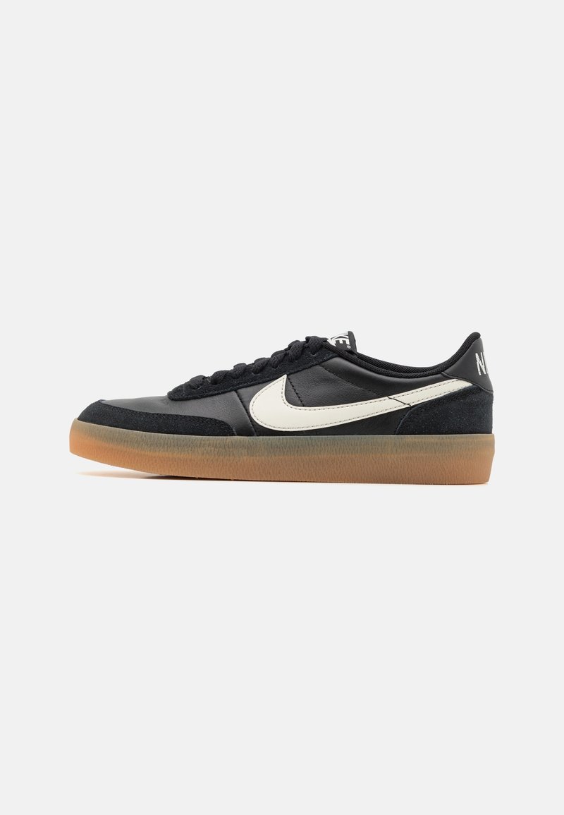 Baskets basses noires avec le swoosh blanc de Nike et une semelle en gomme, vue de côté sur fond gris clair uni.