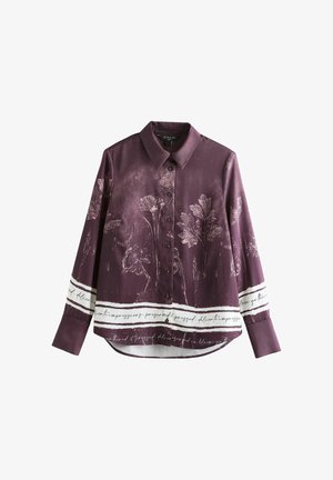 Chemise en soie violette avec un imprimé floral et des accents à rayures blanches portant un texte manuscrit. Fermeture boutonnée à l'avant et manches longues.