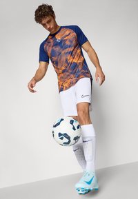Nike athletic shirt in blue with orange abstract design, paired with white shorts, light blue cleats, and a soccer ball.