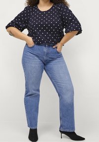 Granatowa bluzka w kropki z bufiastymi rękawami, zestawiona z jasnoniebieskimi prostymi dżinsami i czarnymi szpilkami. Gładka faktura materiału.