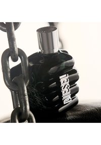 Flacon de parfum en verre noir en forme de poing, avec un capuchon argenté et le logo "DIESEL" embossé en argent d'un côté.