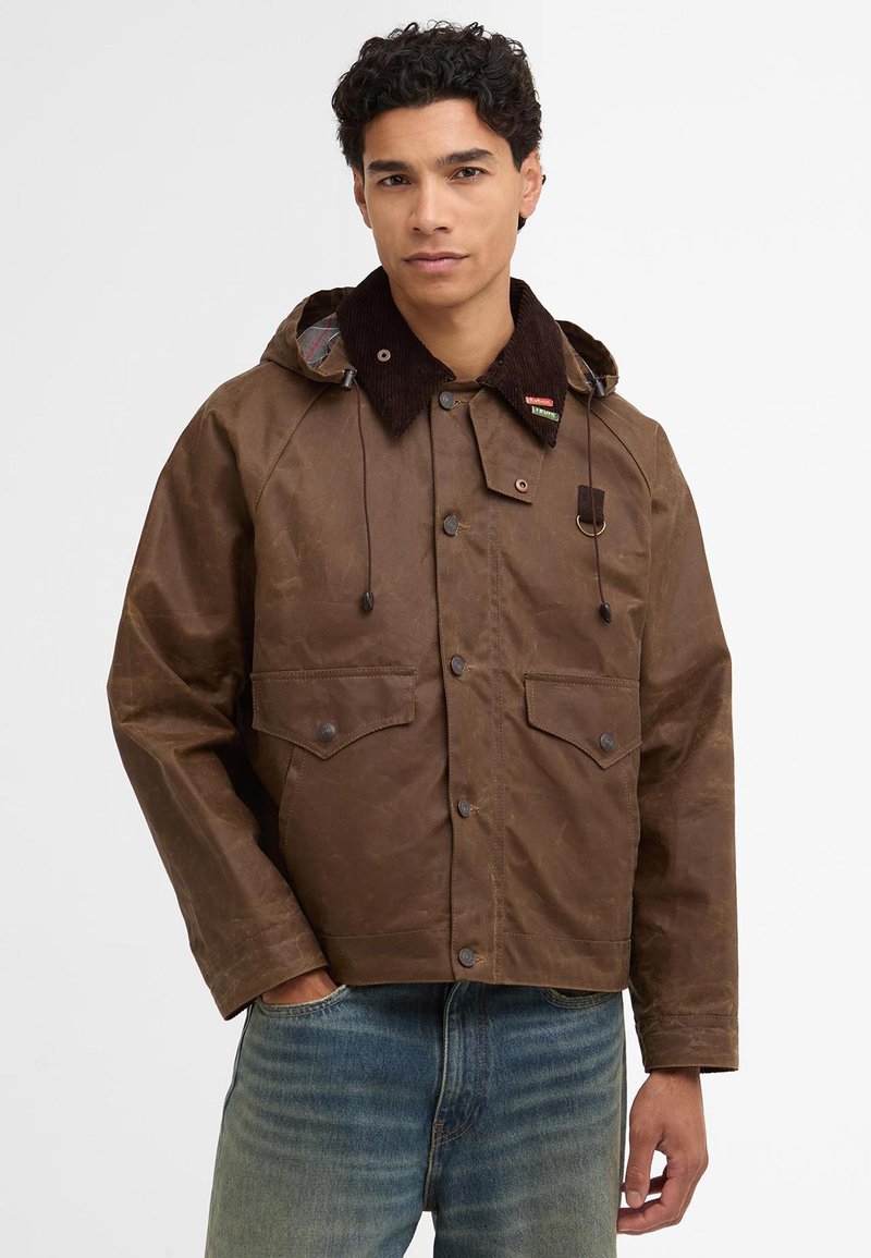 Brown waxed jacket with a corduroy collar, two chest pockets, and drawstring hood. Features a plaid lining and metal hardware accents.