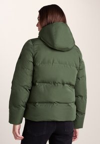 Green puffer jacket with a hood, featuring a quilted design and smooth texture. Includes black logo detail on the left shoulder.
