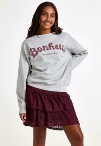 Grauer Sweatshirt mit "Bonheur" in Burgunderrot, kombiniert mit einem mehrlagigen Spitzenrock in Burgunderrot. Das Outfit zeichnet sich durch eine lockere Passform und strukturierten Stoff aus.