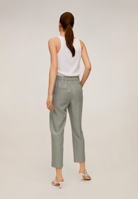 Pantalon gris clair, ajusté, avec une taille élastique, associé à un débardeur blanc et des sandales blanches à talons. Texture de tissu lisse.