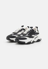 Chunky black and white sneakers featuring mesh panels, lace-up design, rubber outsole, and prominent branding on the side.