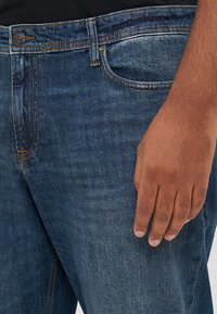 Dark blue denim jeans with a classic fit, featuring a zipper fly, front pockets, and distinctive stitching details along the seams.