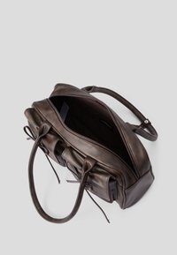 Brun lærveske med en strukturert design. Har doble håndtak, glidelås og dekorative knuter på sidene. Innsiden er mørk.
