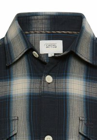 Koszula na guziki w kratę w odcieniach granatu, kremu i niebieskiego, z miękką fakturą, klasycznym kołnierzem oraz dwoma zapinanymi na guziki kieszeniami na piersi.