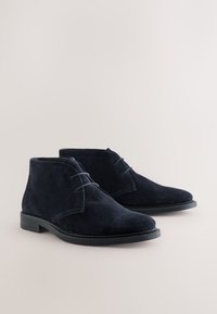 Marineblaue Wildleder-Desert-Boots mit abgerundetem Zehenbereich, Schnürdesign und flachen Gummisohlen, mit sichtbaren Nahtdetails.