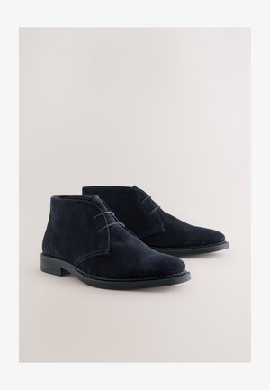 Pustinjske čizme od teget plave brušene kože s zaobljenim vrhom, vezicama i ravnim gumenim potplatima, s vidljivim ukrasnim šavovima.