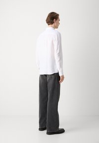 Weißes Leinenhemd mit langen Ärmeln und Knopfmanschetten, kombiniert mit einer lockeren dunkelgrauen Jeans. Einfaches Design mit entspanntem Schnitt.