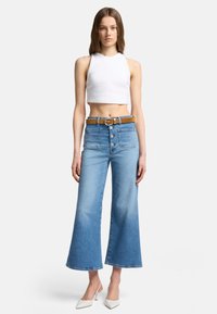 Lyseblå høymidjede bukser med flagrende bein, frontknapper, et brunt belte og en hvit kortermet topp uten ermer. Glatt denimtekstur.