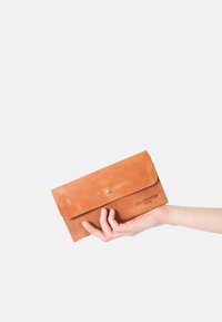 Brown leather wallet with a flap closure, brass button, and embossed logo. Handheld, features smooth texture and simple rectangular design.