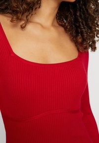 Top rosso a coste con scollatura quadrata e maniche lunghe, realizzato in tessuto testurizzato e design aderente, ideale per essere indossato a strati.