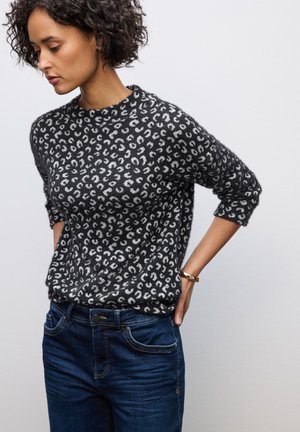 Maglione a motivi in bianco e nero con collo rotondo, maniche a tre quarti e una vestibilità ampia, abbinato a jeans di un blu scuro.