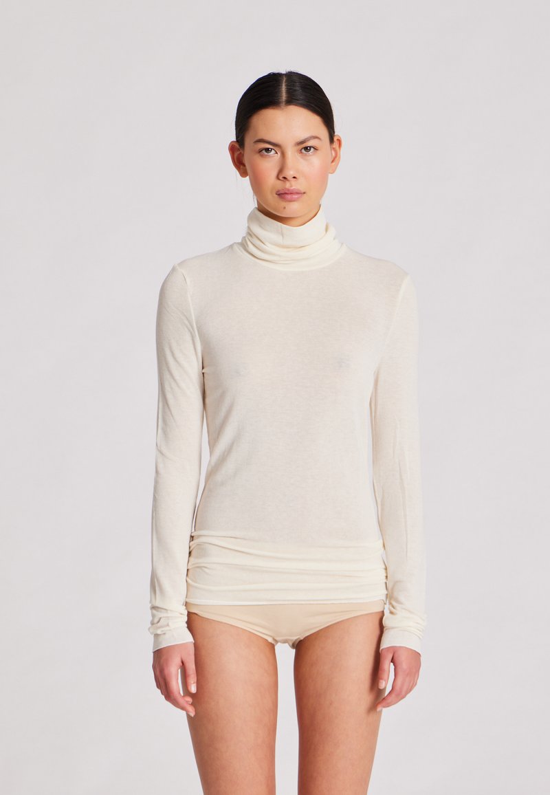 Langärmliges Rollkragenoberteil in Creme, aus leichtem Stoff mit glatter Textur; zeichnet sich durch eine figurbetonte Silhouette und geraffte Saumdetails aus.