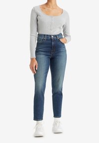 Ljusgrå ribbad långärmad topp med rund halsringning och knappdetalj, tillsammans med högmidjade blåjeans och vita sneakers.