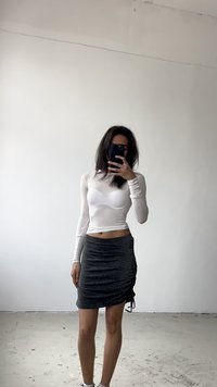 Top alb cu mâneci lungi, asortat cu o fustă mini gri cu ajustări, purtat cu adidași albi. Texturi netede, design ajustat.